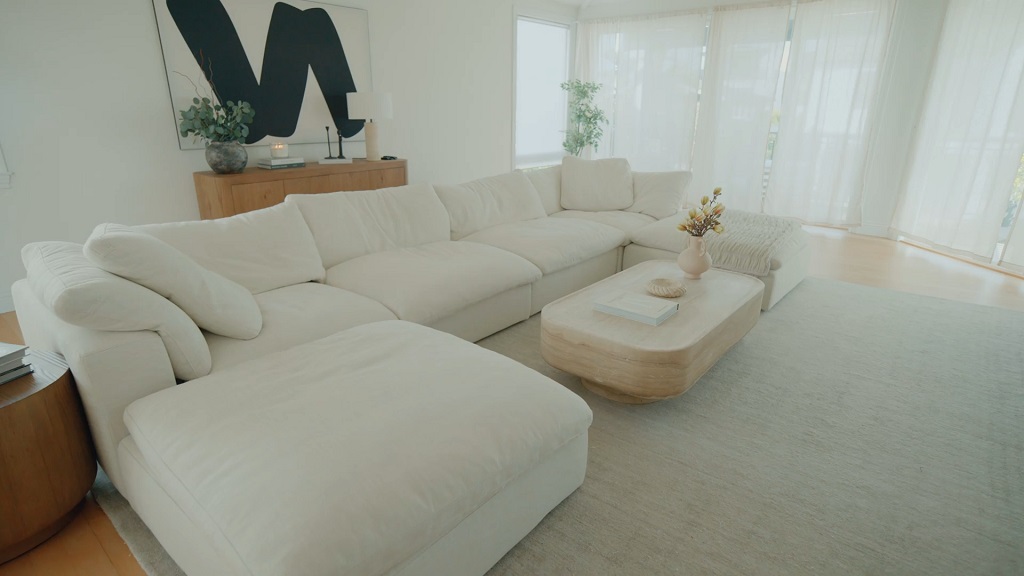 Small living area styled in soft neutral tones with a light sectional sofa, sheer curtains, and uncluttered surfaces